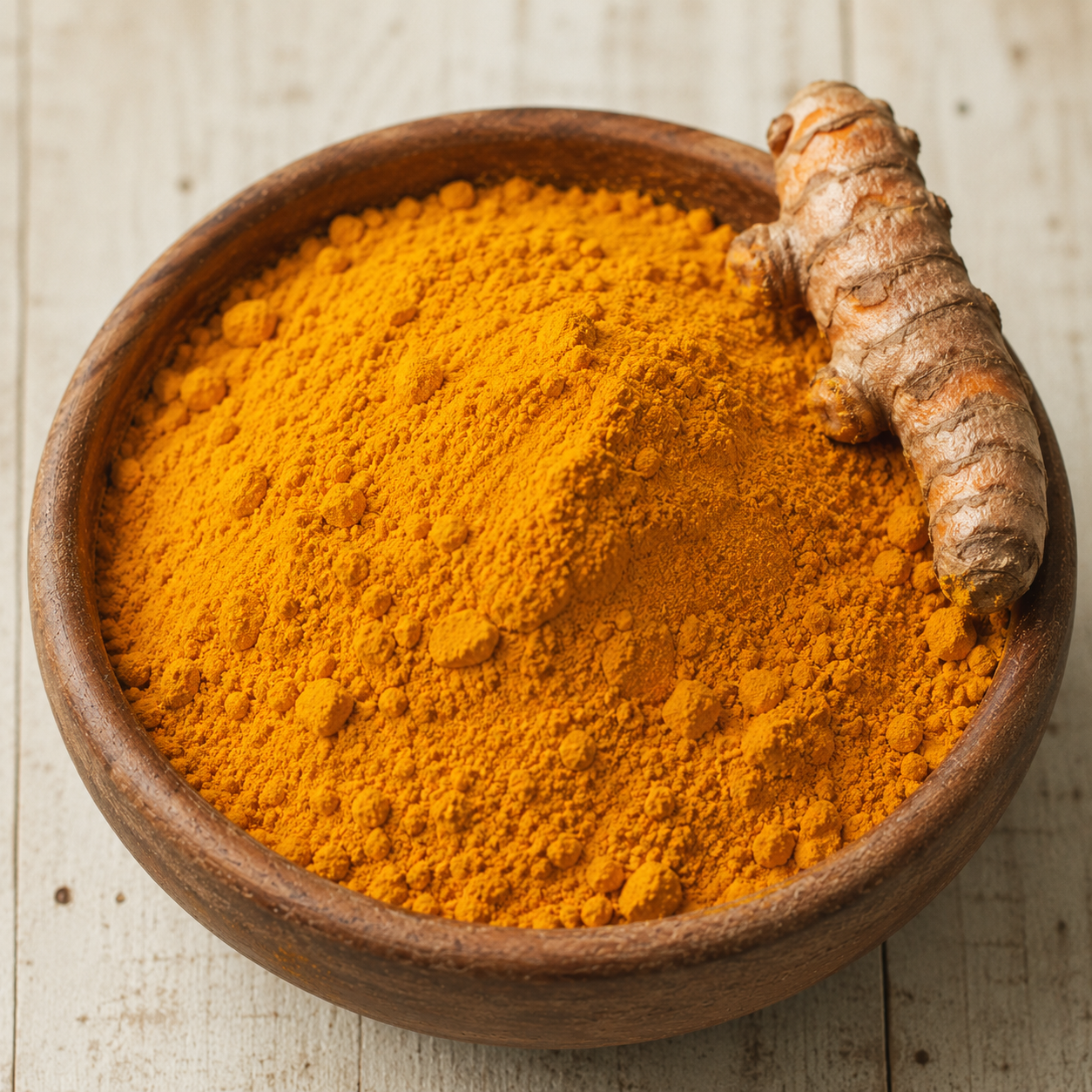 Ground turmeric in a wooden bowl with fresh rhizome